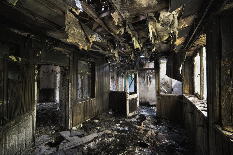 A Complete Guide What to Consider When Purchasing a Fire-Damaged Property An inside shot of an abandoned destroyed building with burned walls and worn-out doors